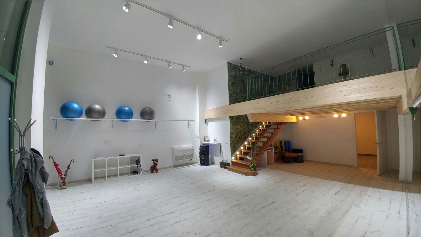 Ampio ambiente chiaro con soppalco, scala in legno e illuminazione al soffitto.