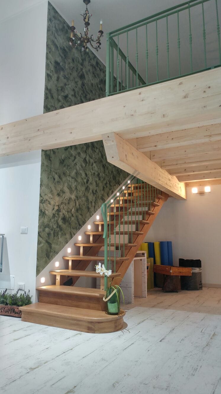 Scala interna in legno con parete decorativa verde e punti luce sulla parete vicina.