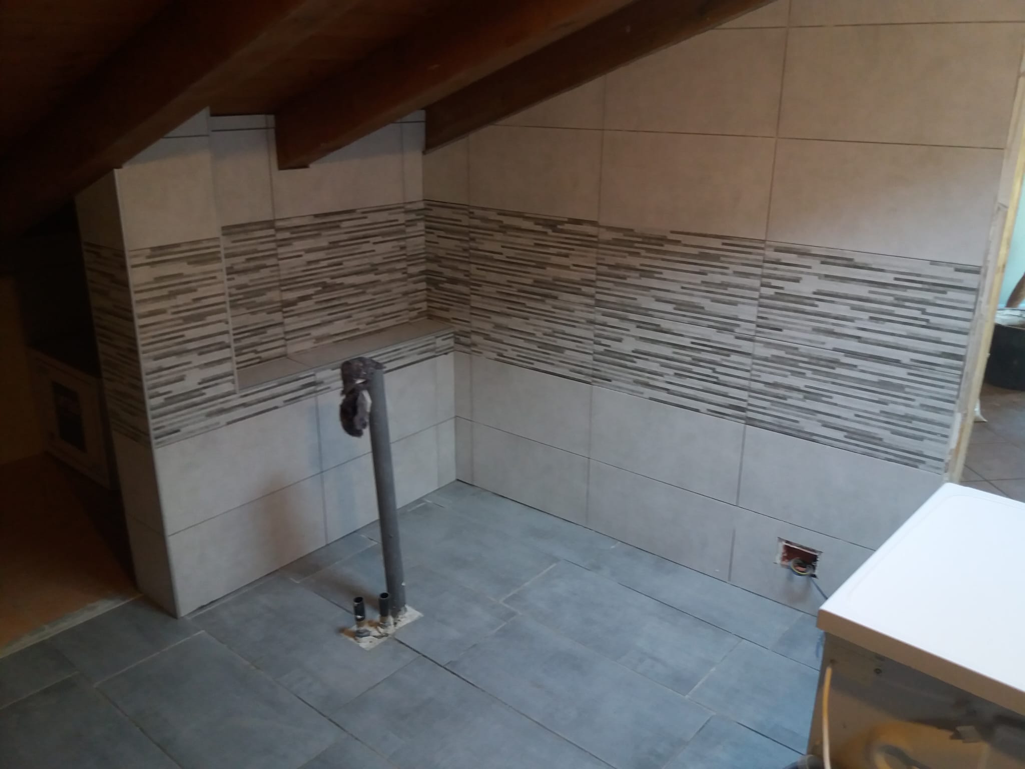 Bagno con soffitto in legno a vista, pareti chiare e fascia orizzontale decorativa.